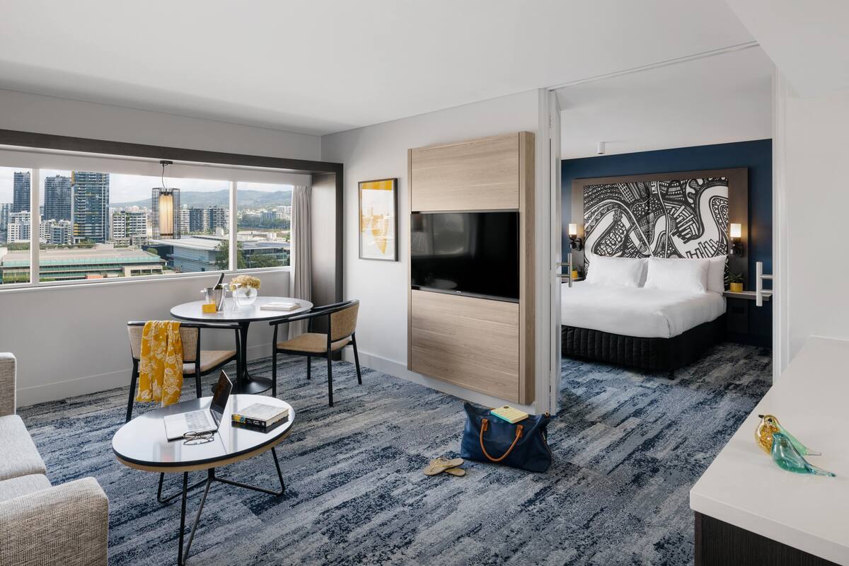 A hotel room with a city view, a bed, a desk, a chair, a table, and a TV.