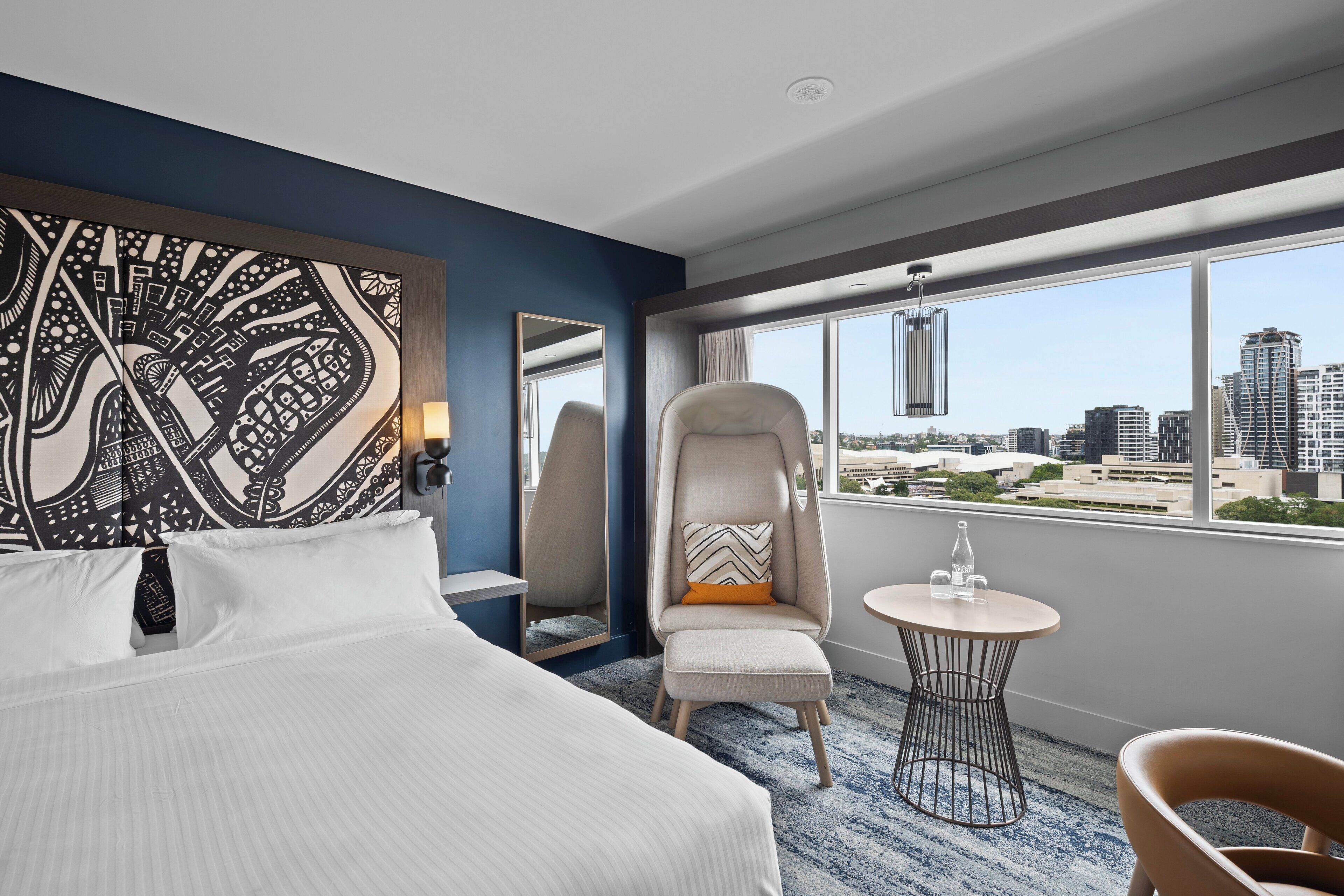 Habitación de hotel con una cama grande, una silla, una mesita y vistas a la ciudad.