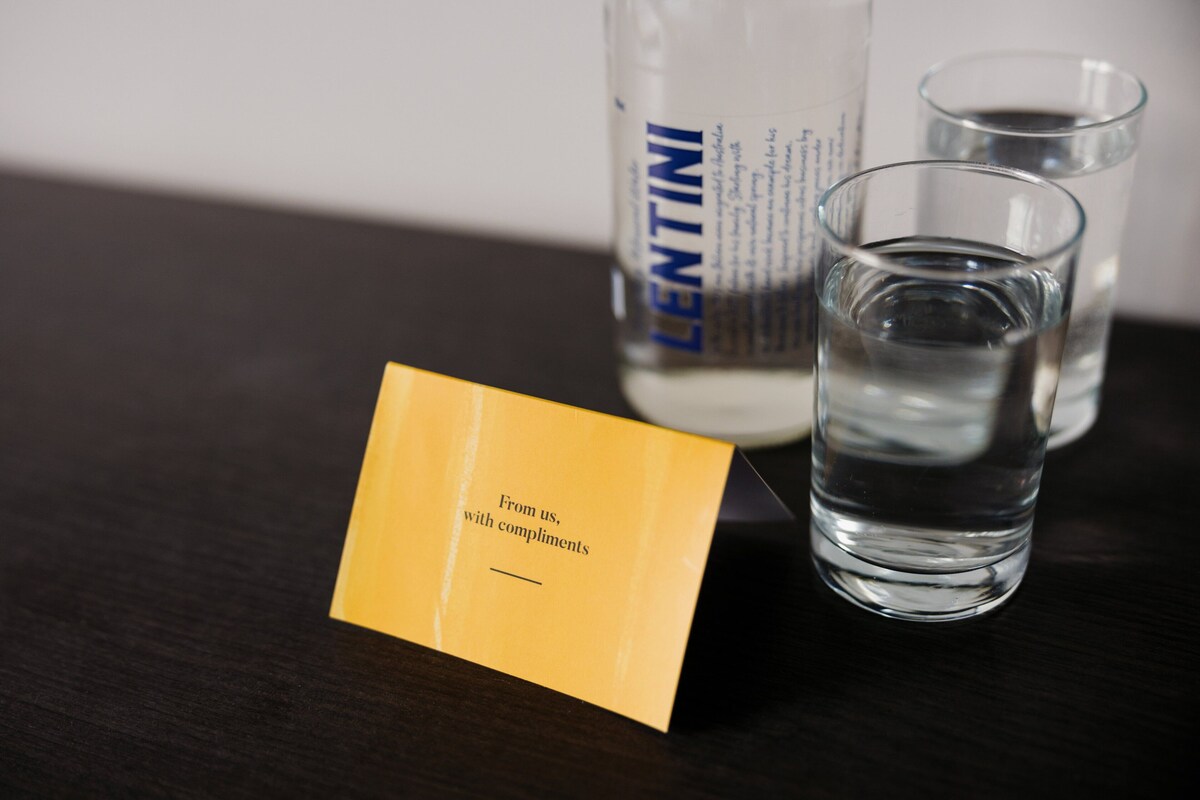 A bottle of LENTINI water, a glass with water, and a yellow card with text.