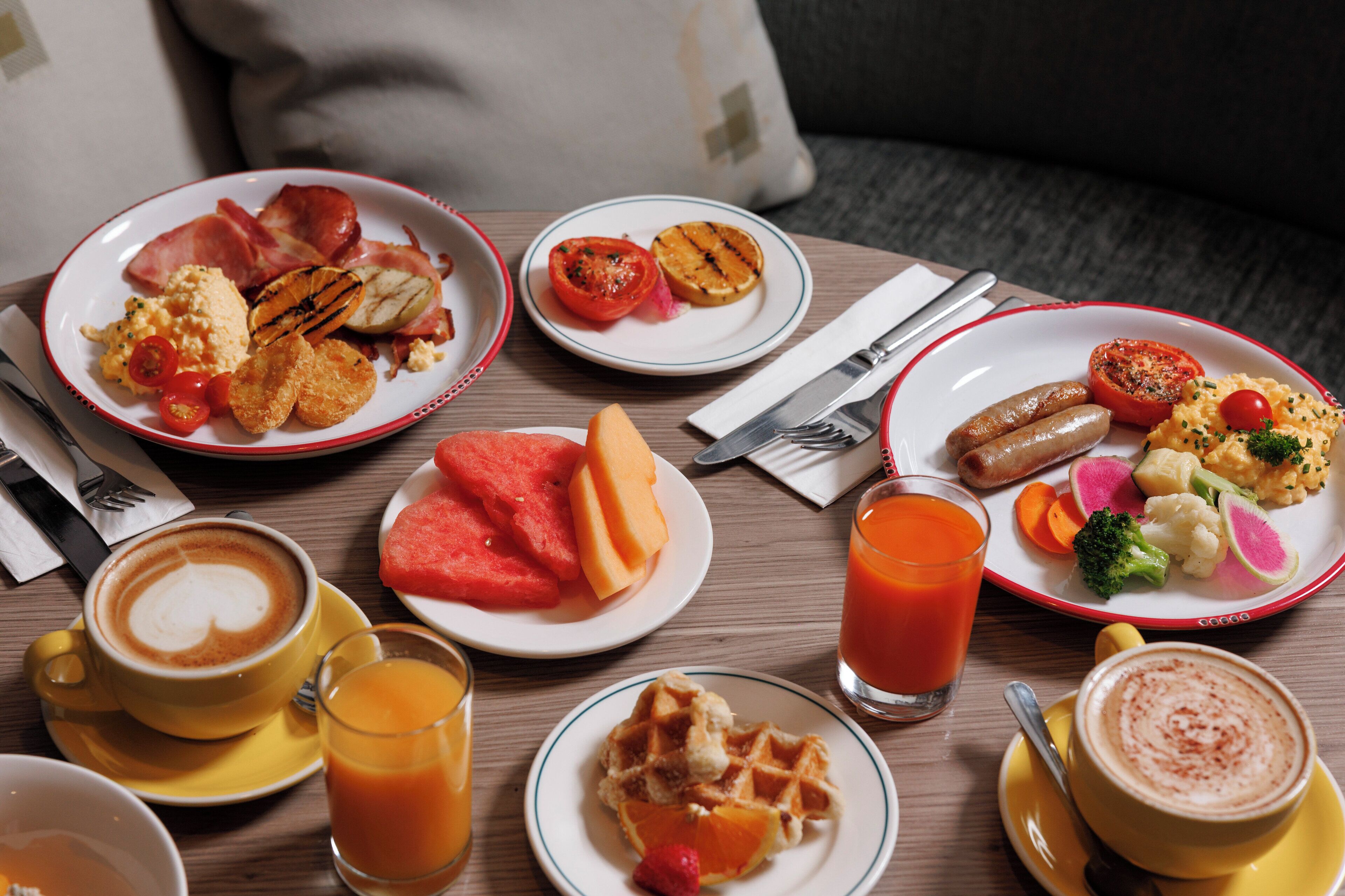 A breakfast table with plates of food, a coffee cup, and a glass of orange juice.
