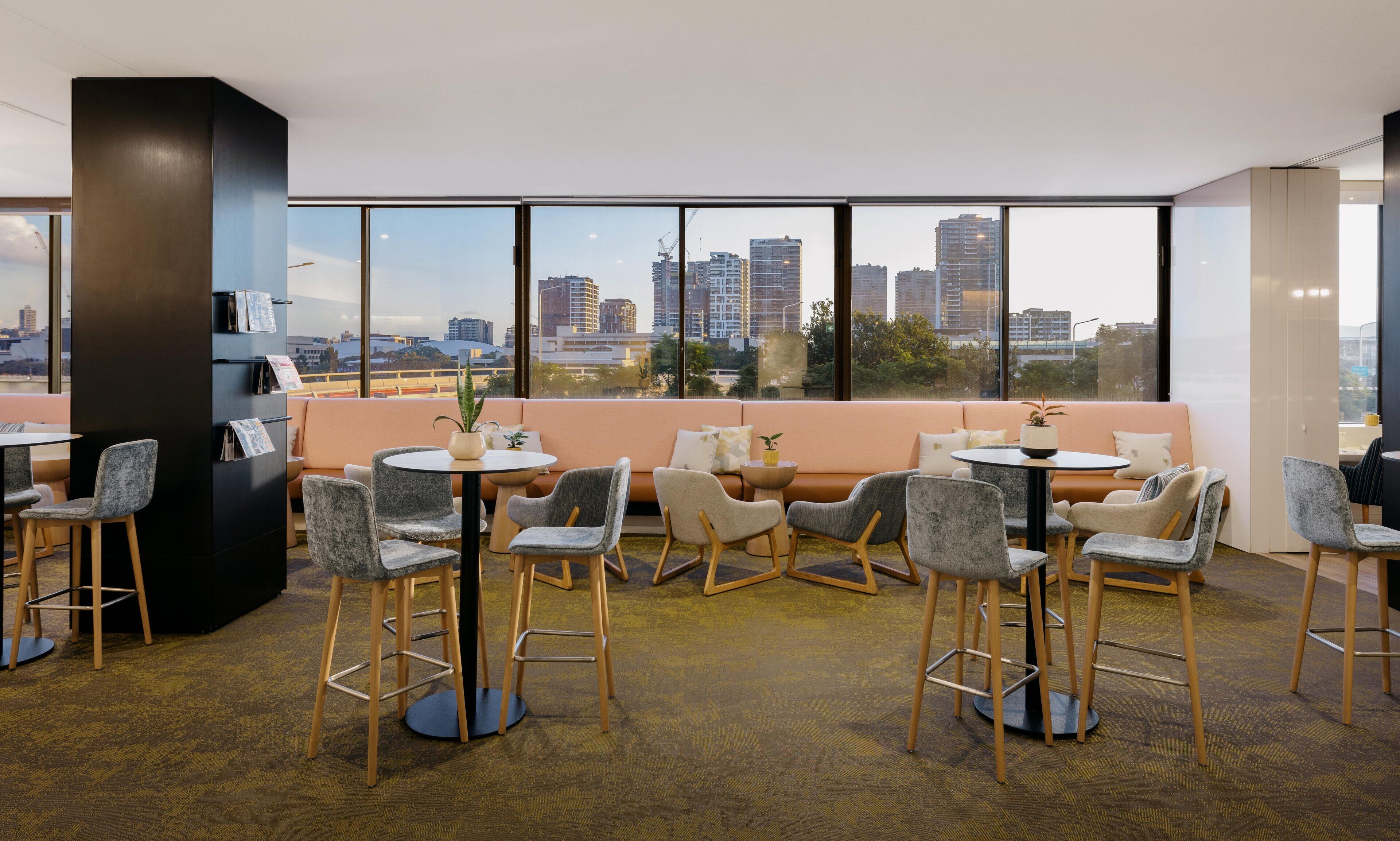 Un espace lounge moderne avec vue sur la ville, comprenant un canapé, des tables rondes et des tabourets de bar.