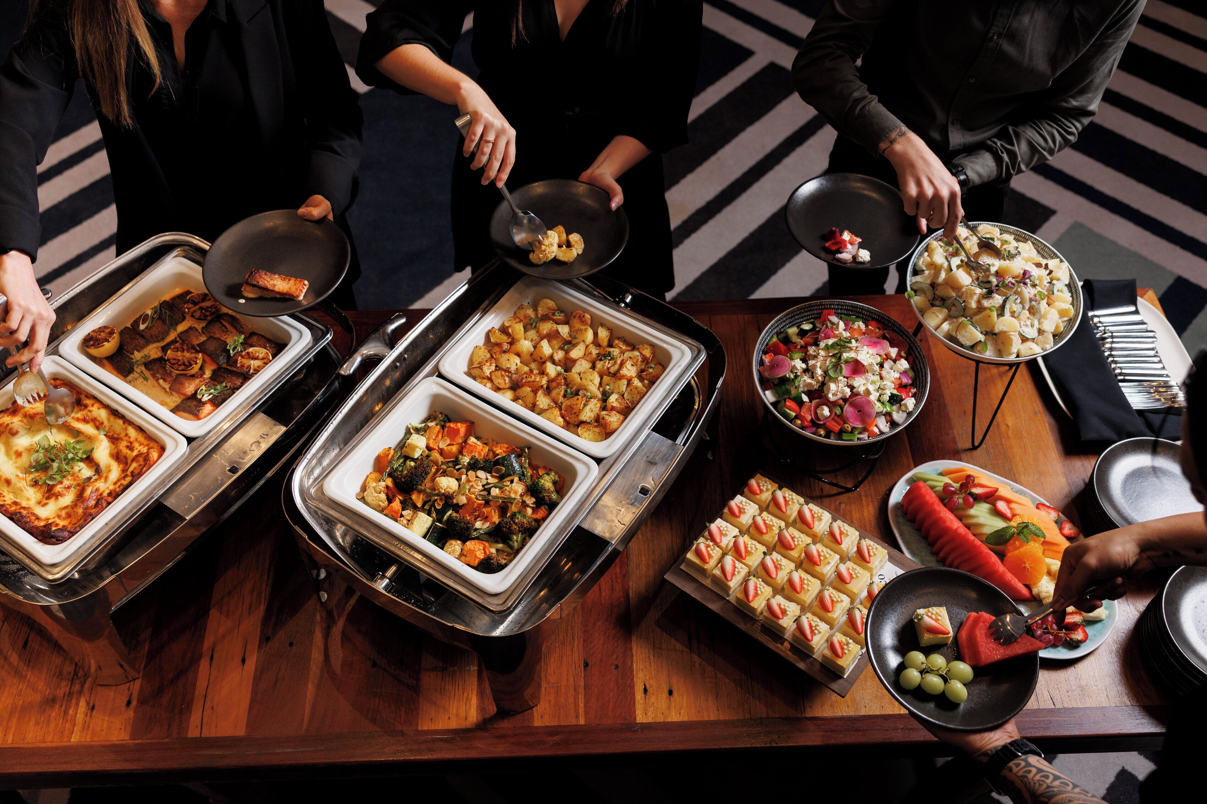 Mesa de buffet com diversos alimentos e uma pessoa servindo.