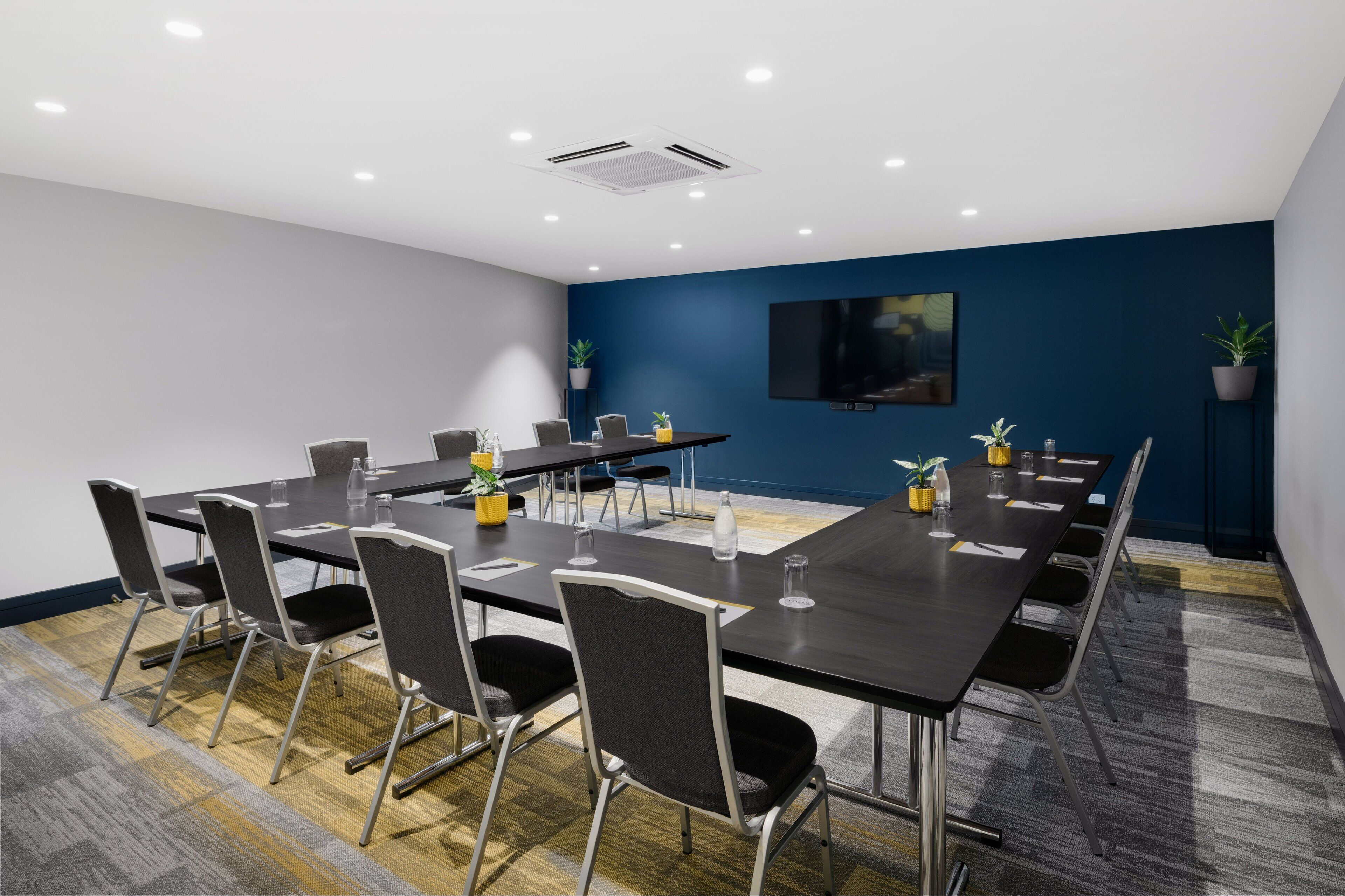 A conference room with a long table, chairs, a flat-screen TV, and potted plants.