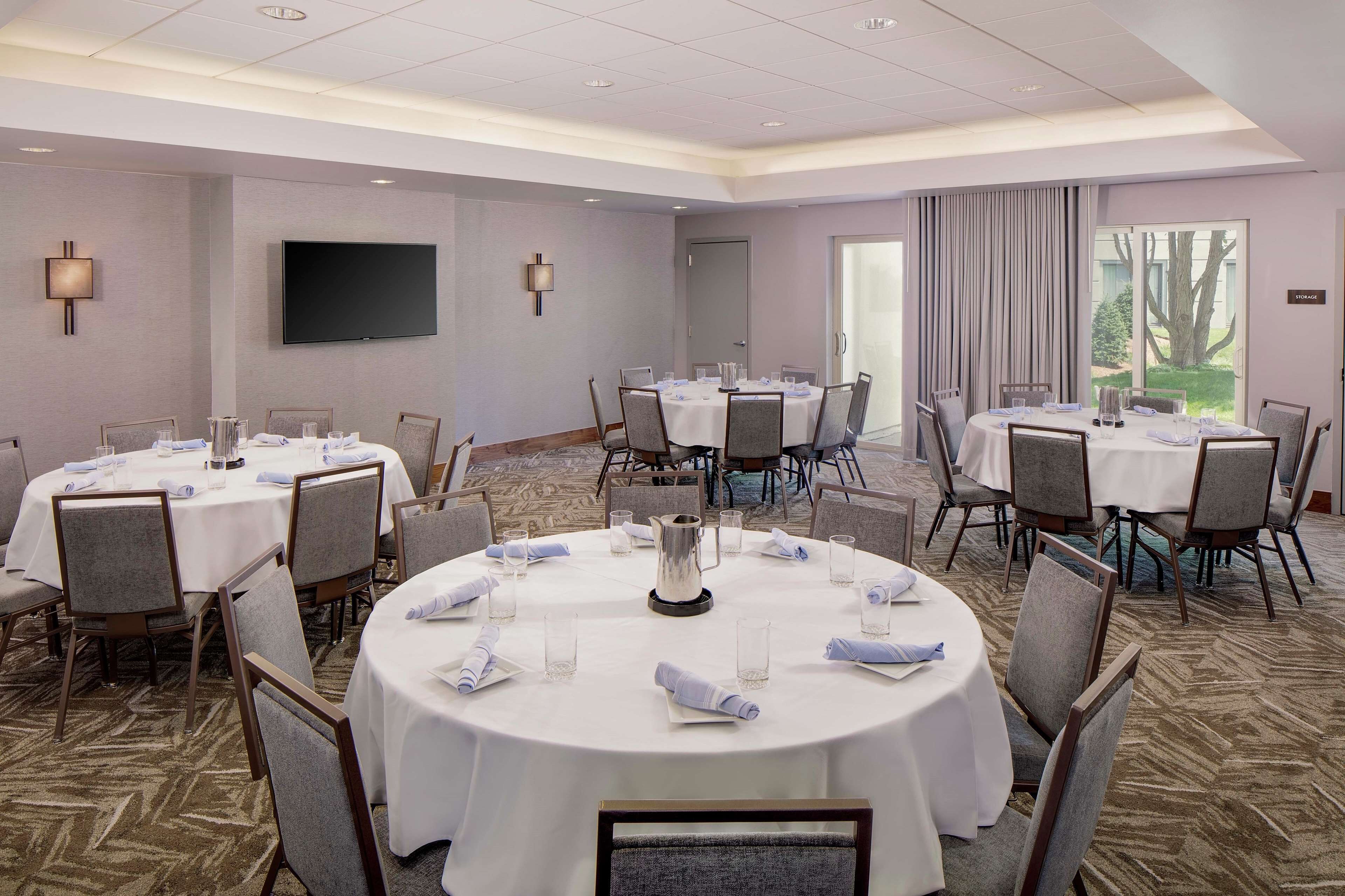 A conference room with multiple round tables, each set with chairs, glasses, and napkins.