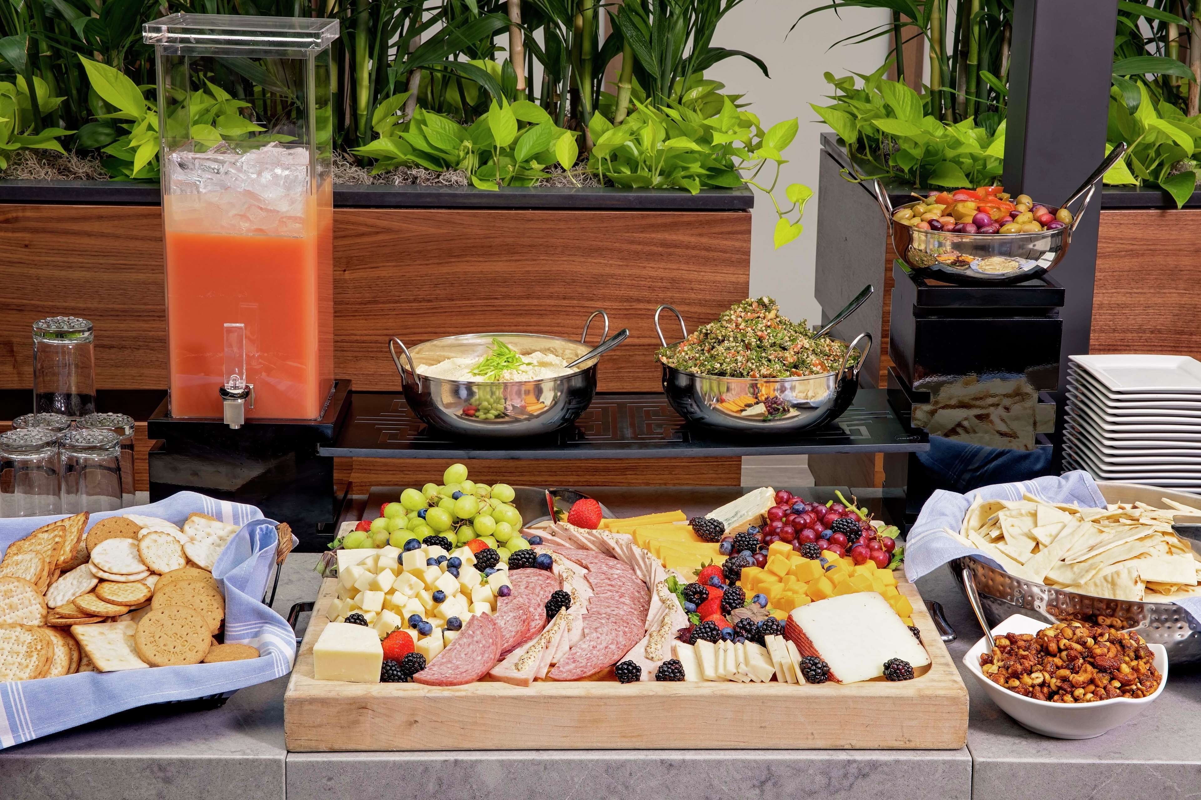 A buffet with various food items including fruits, cheeses, meats, and a drink dispenser.