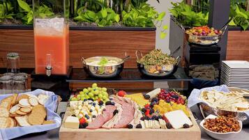 A buffet with various food items including fruits, cheeses, meats, and a drink dispenser.