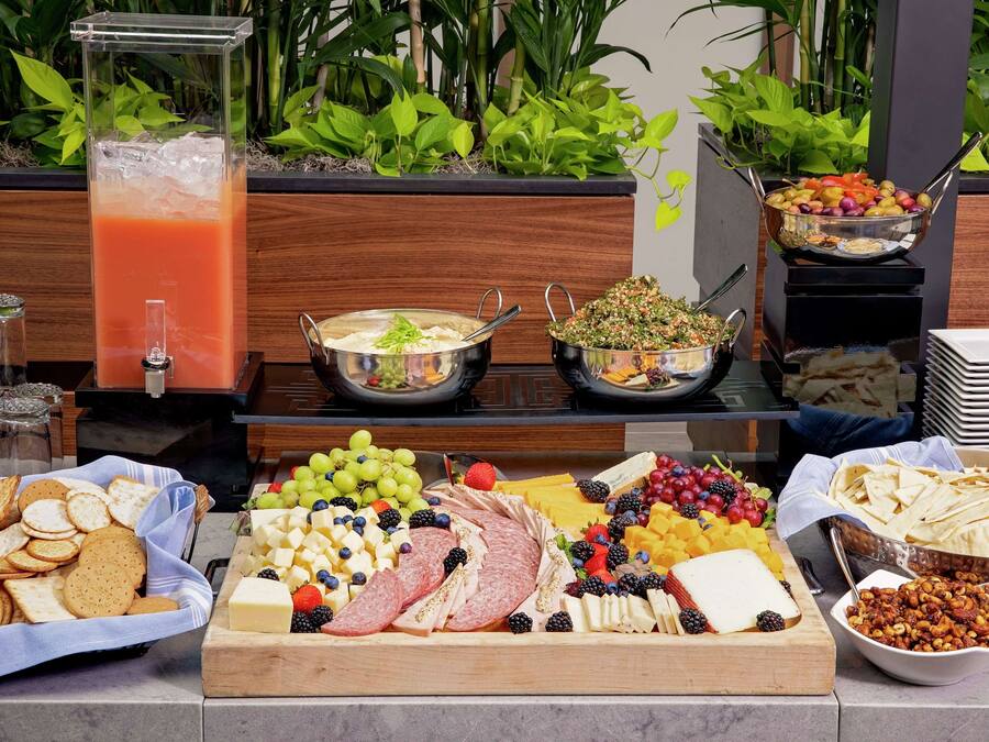 Ein Buffet mit verschiedenen Speisen, darunter Obst, Käse, Fleisch und einem Getränkespender.
