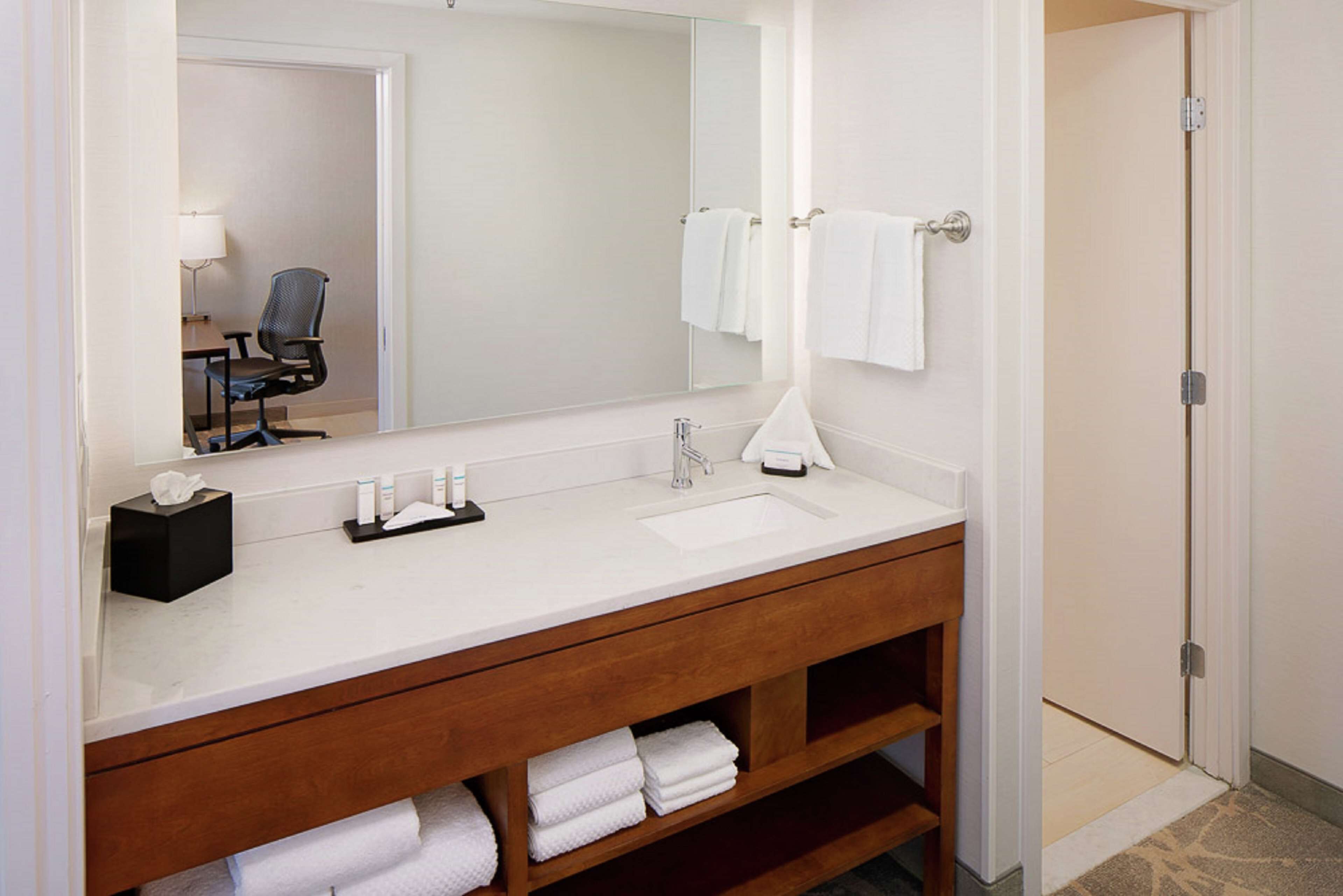 A bathroom with a white sink, wooden vanity, and a large mirror. There are towels and toiletries on the counter.