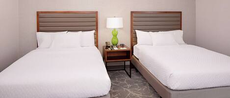 A hotel room with two beds, a nightstand with a lamp, and a carpeted floor.
