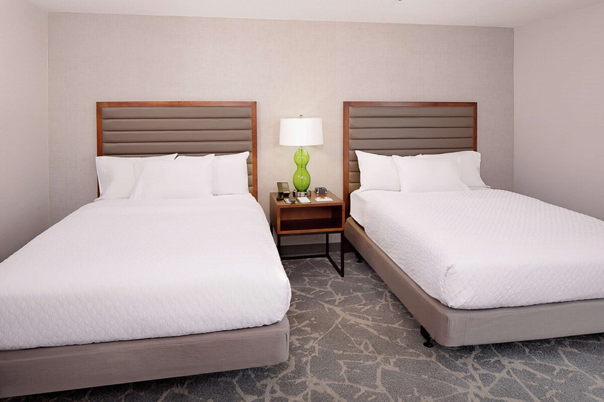 Two adjacent beds with wooden headboards, a nightstand with a green lamp, and a patterned carpet.