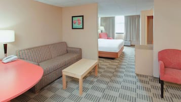 Una habitación de hotel con un sofá estampado, una mesita, una cama y un sillón rojo.