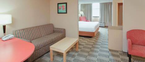 A hotel room with a patterned sofa, a small table, a bed, and a red armchair.