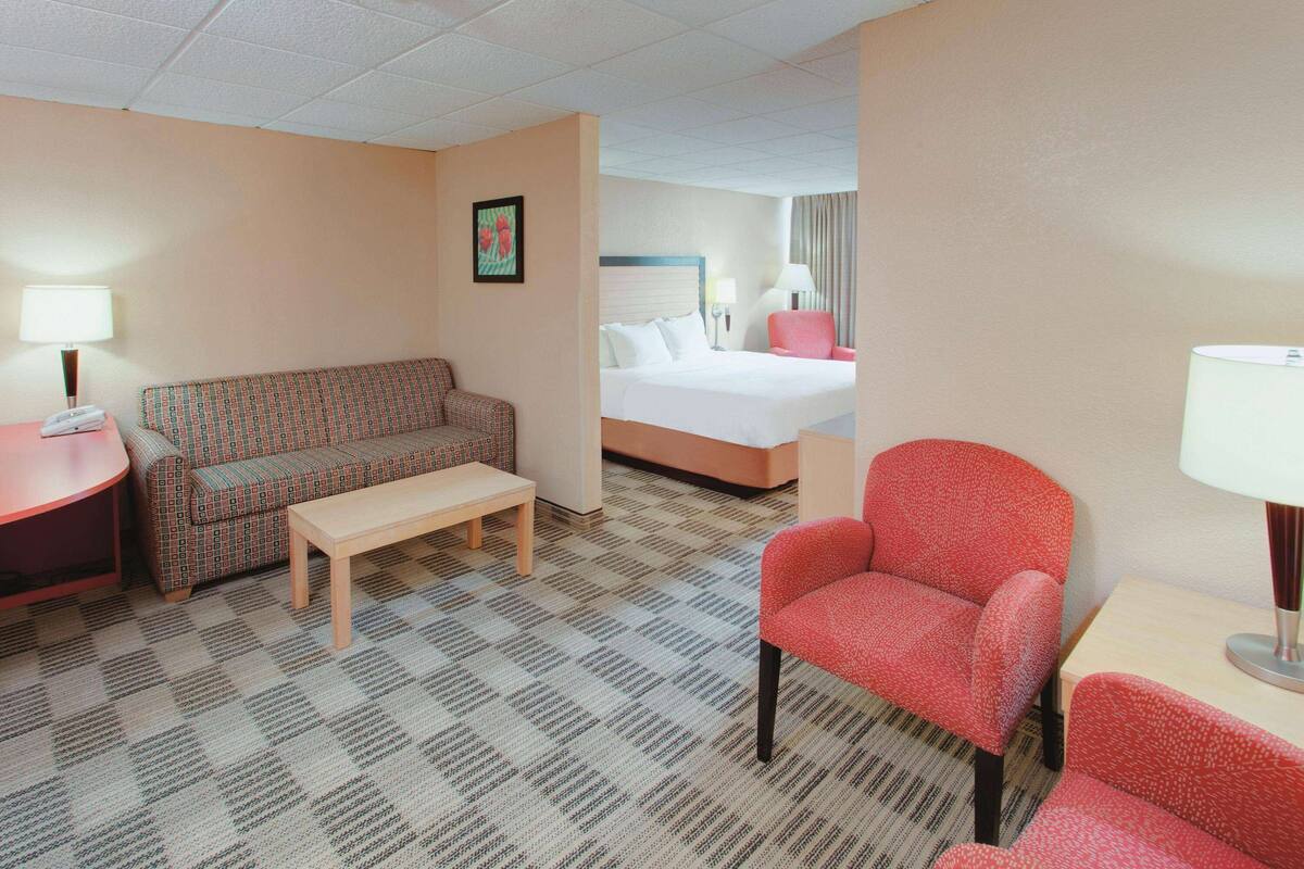 Una habitación de hotel con cama, sofá, sillón, mesa y lámpara.