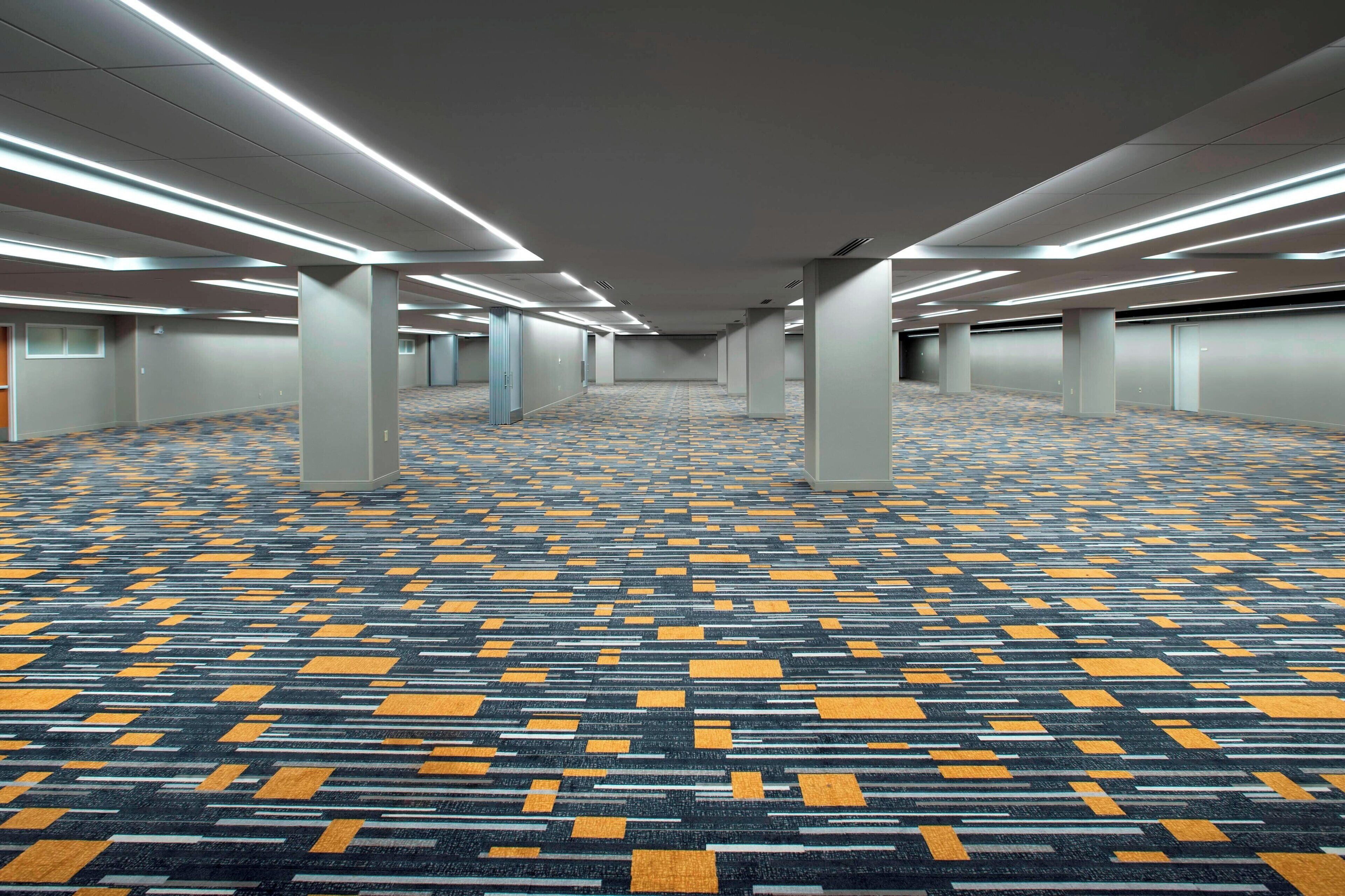 A spacious hotel corridor with patterned carpet, ceiling lights, and columns.