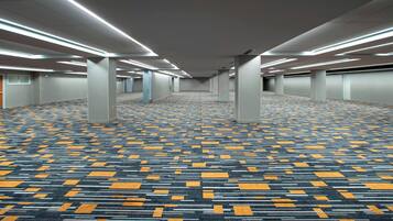 A spacious hotel corridor with patterned carpet, ceiling lights, and columns.