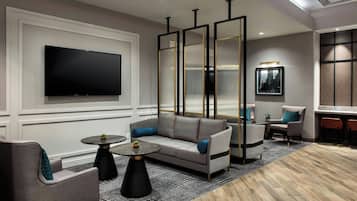 Een moderne woonkamer met een bank, fauteuils, een salontafel en een aan de muur bevestigde televisie.