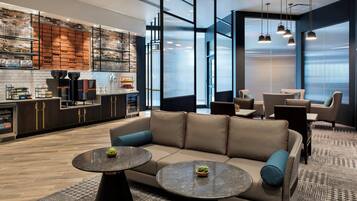 Ein stilvoller Loungebereich mit einer Couch, zwei runden Tischen und einer Bar mit Regalen und Küchengeräten.