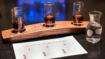 A wooden tray holding four shot glasses with a menu card and a bottle of water on a dark countertop.