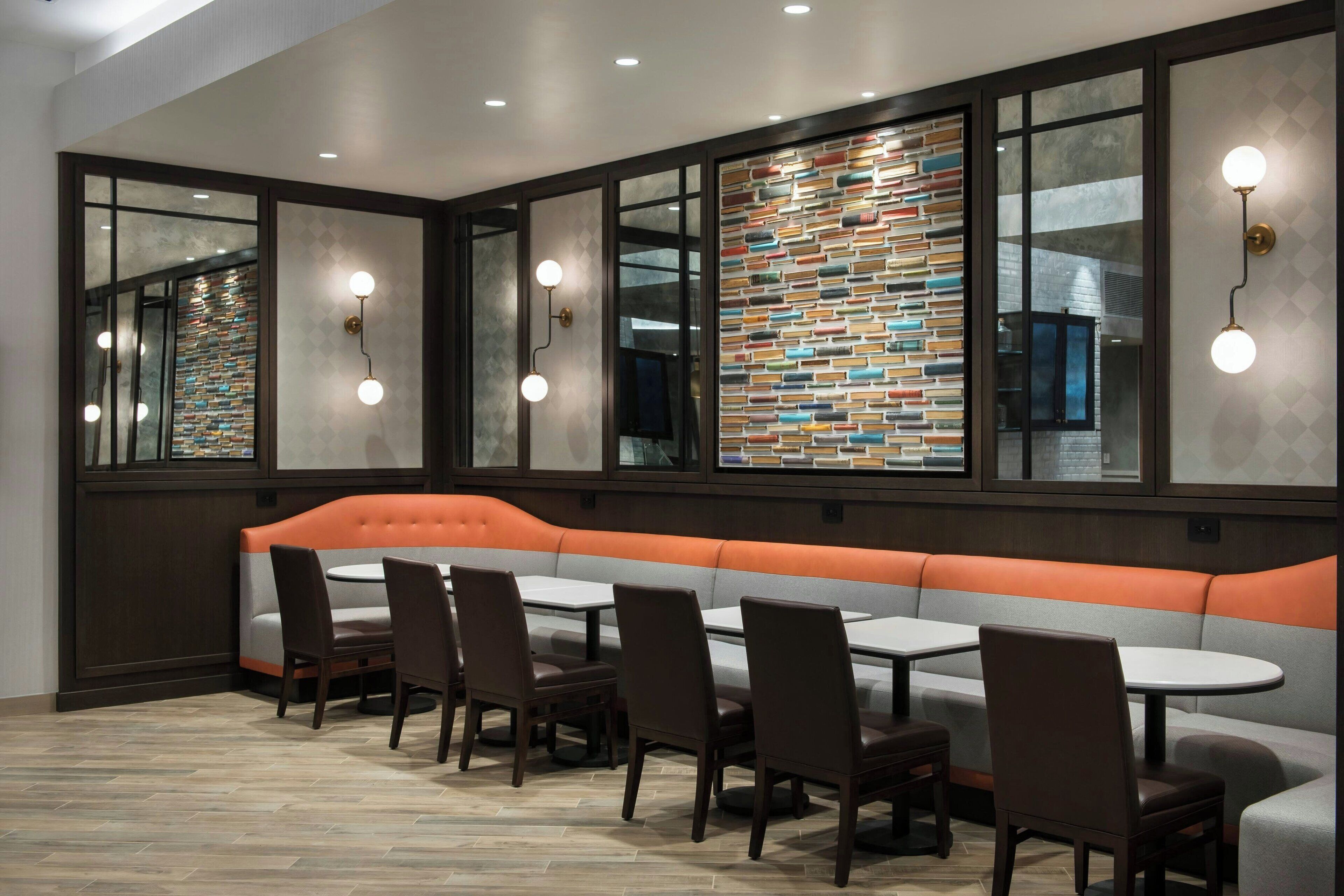 A restaurant with a long orange cushioned bench, multiple tables, and chairs.