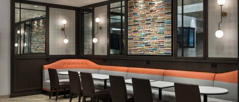A restaurant with a long orange cushioned bench, multiple tables, and chairs.