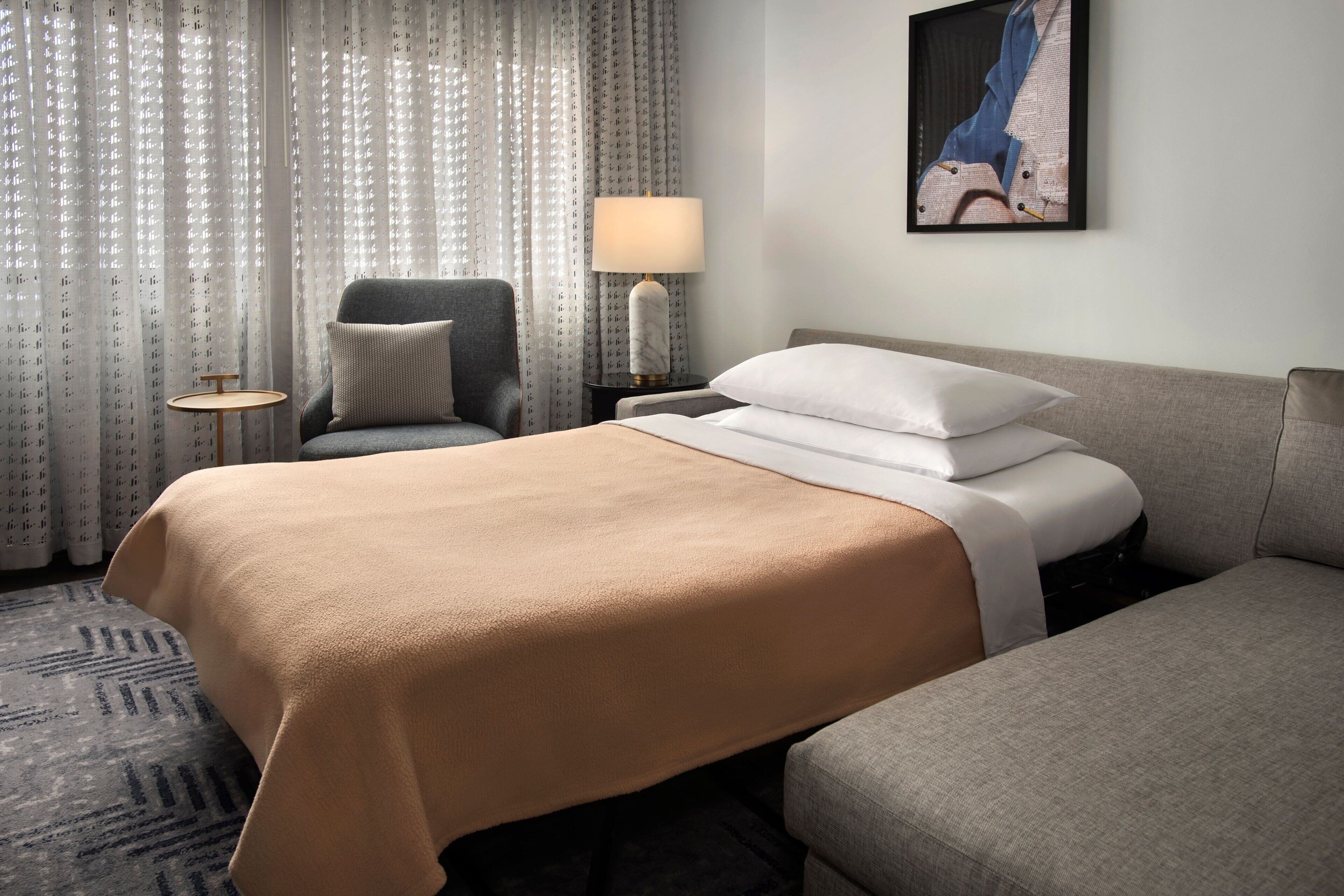 A hotel room with a large bed, a chair, a small table, and a lamp.