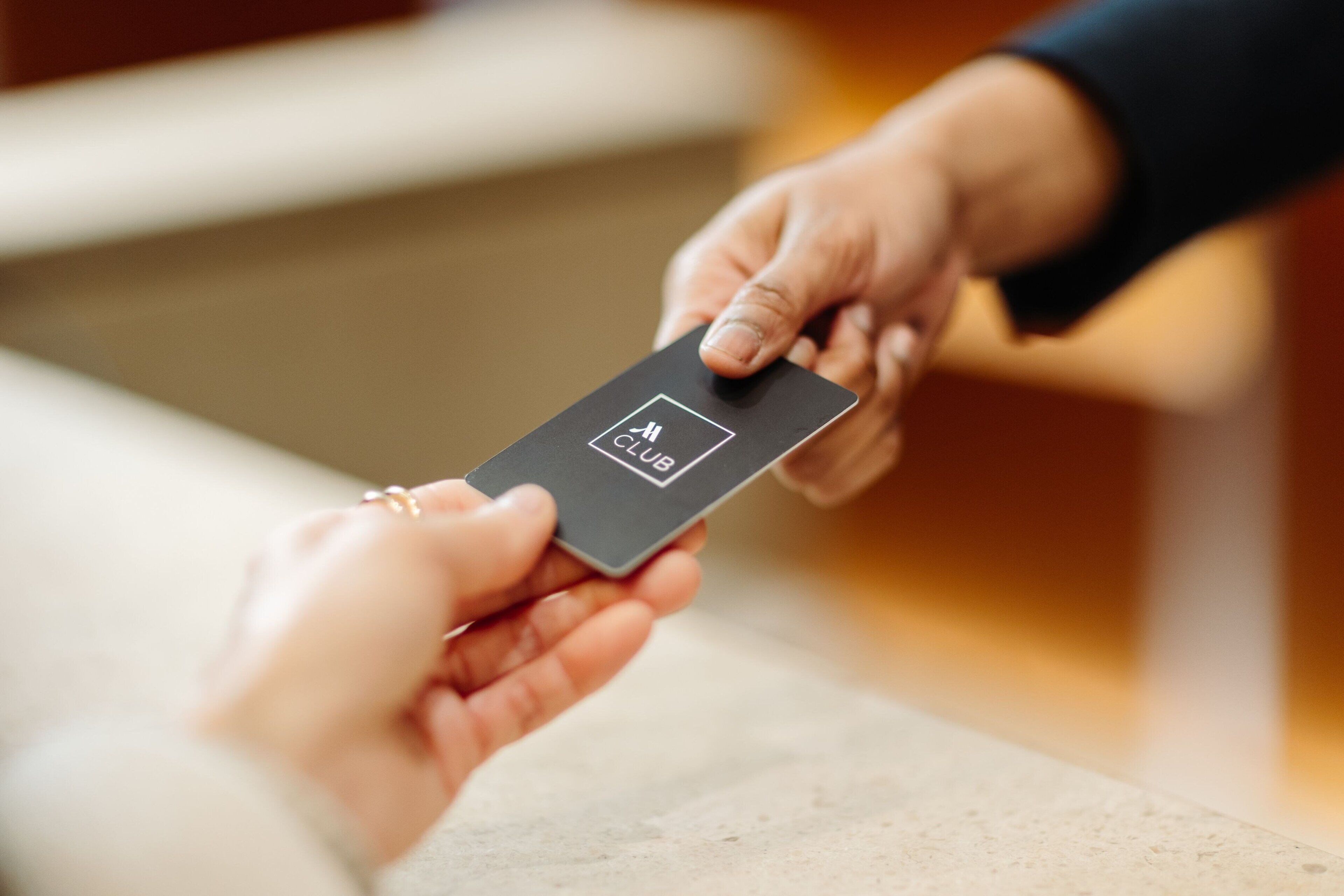 A person handing over a black card with a logo to another person.