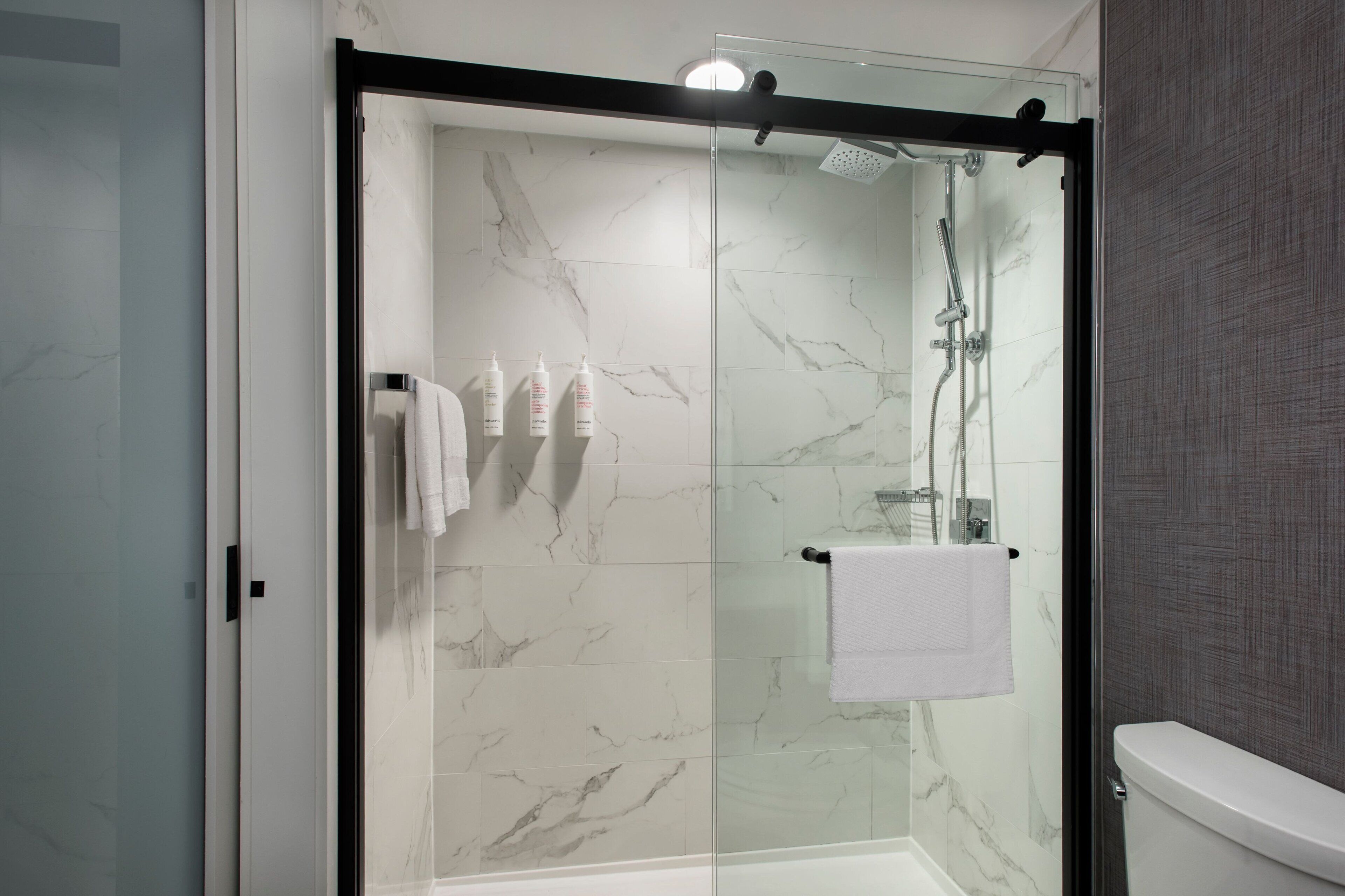 A glass-enclosed shower with a white marble wall, a glass door, and a white towel hanging on the wall.