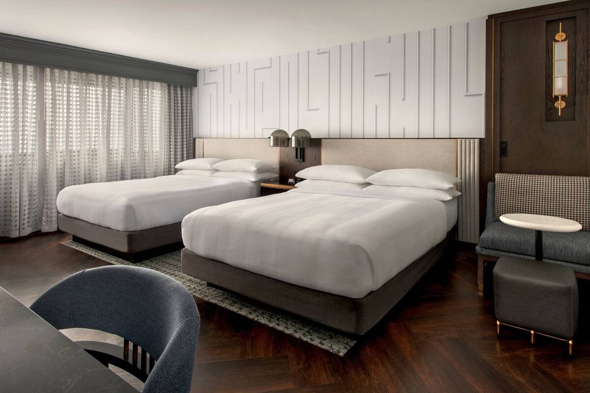 A hotel room with two beds, a desk, and a chair.