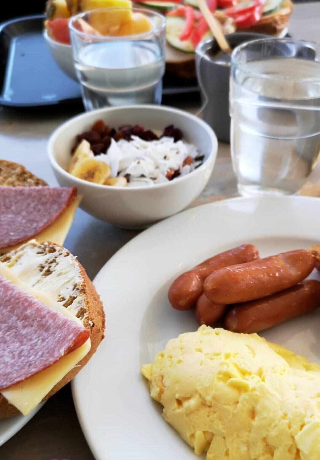 A meal with hot dogs, scrambled eggs, and a bowl of fruit salad.
