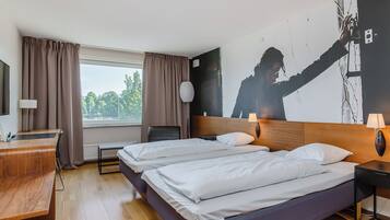 Habitación de hotel con dos camas, un escritorio, una silla, una ventana con cortinas y una pared con una obra de arte grande.
