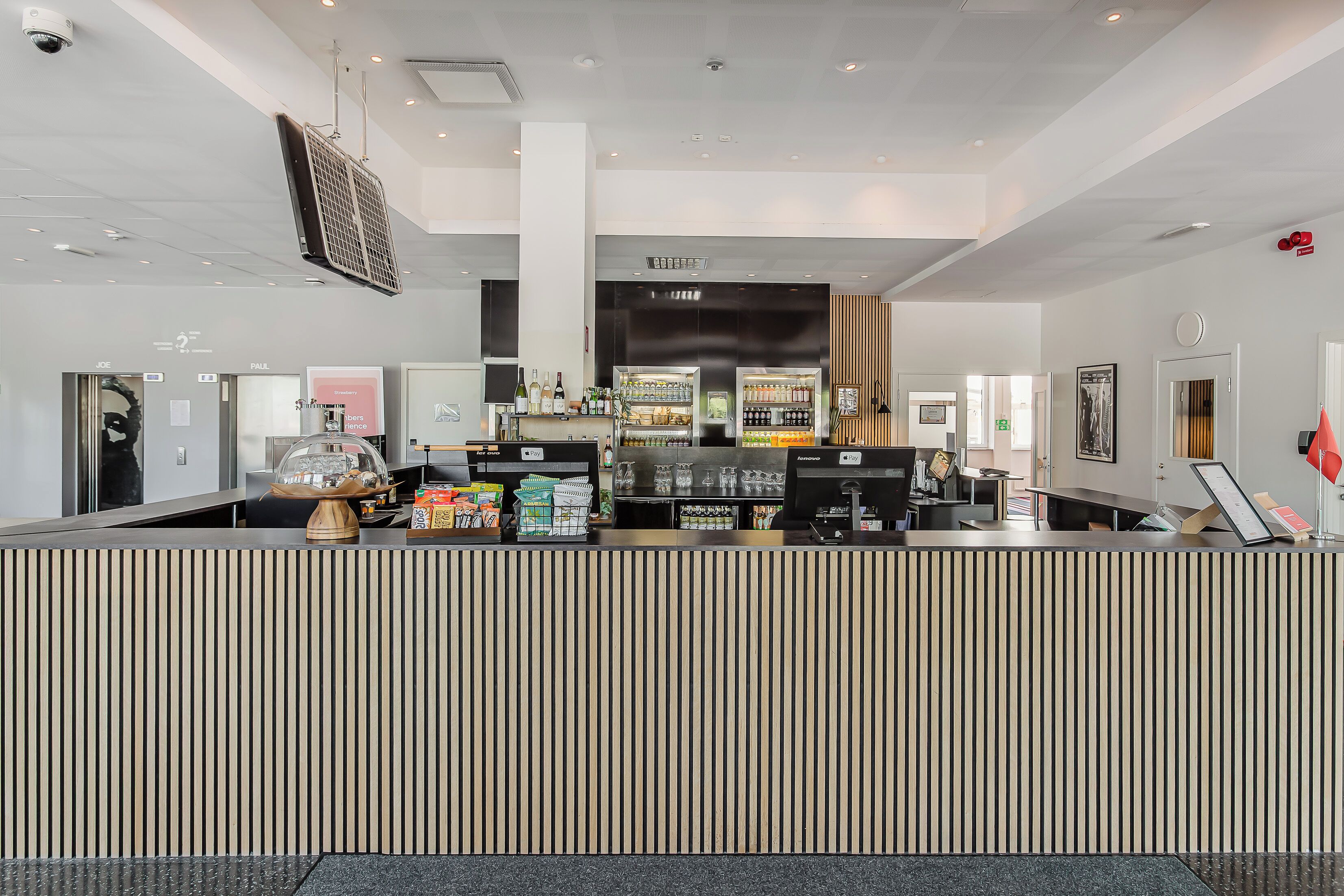 Een moderne hotel receptie met een gestreepte balie, een koffieapparaat en een presentatie van flessen water en snacks.