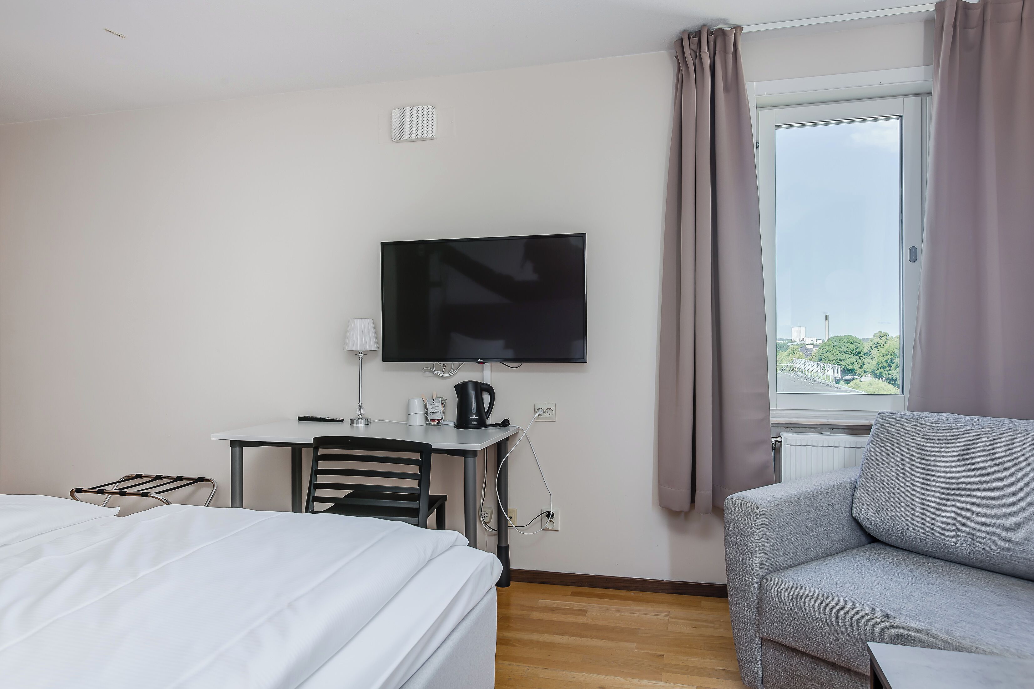 Habitación de hotel con cama, escritorio con silla, televisor y ventana con cortinas.