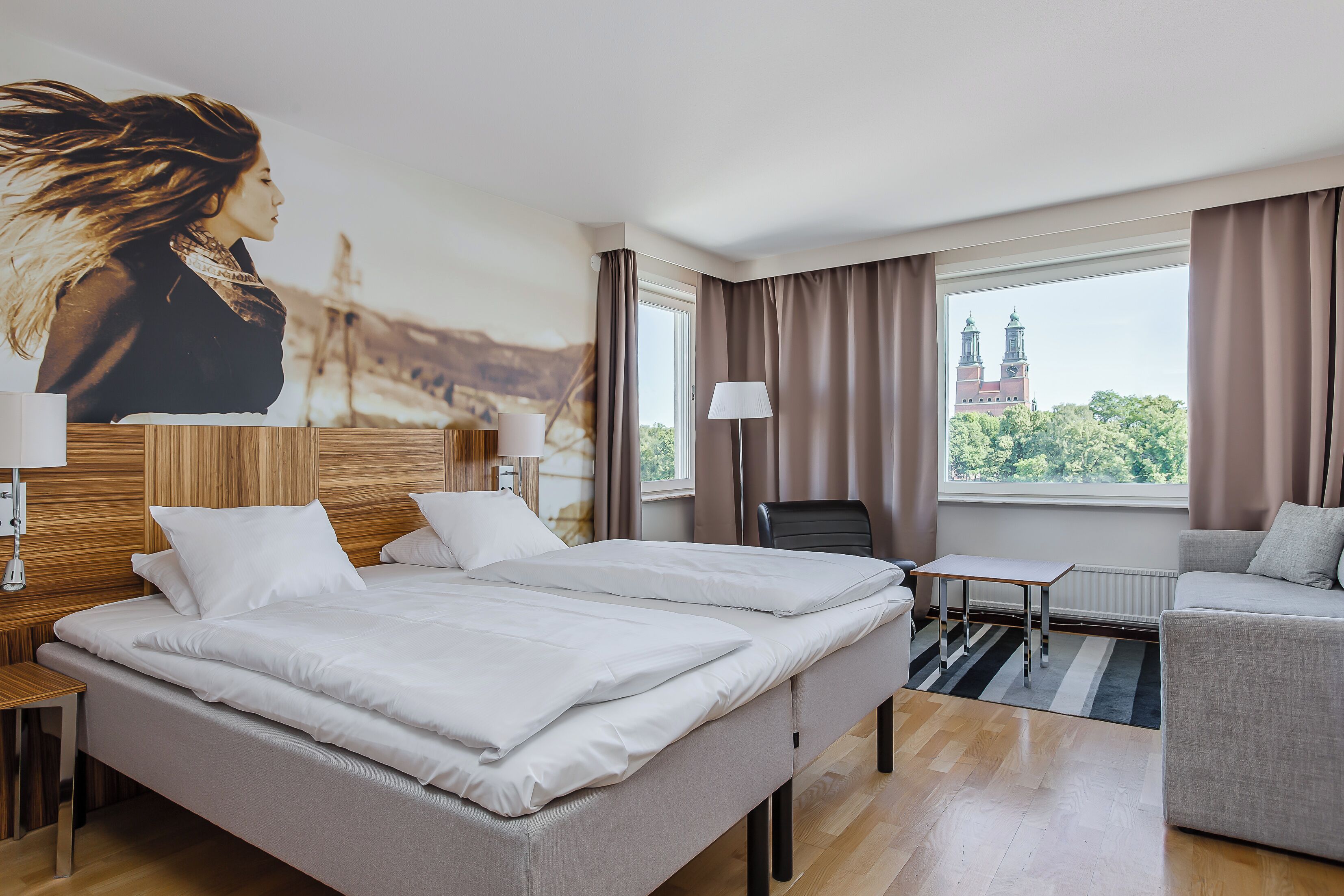 Camera d'albergo con un letto, un divano, un tavolino e vista sulla città con un campanile.