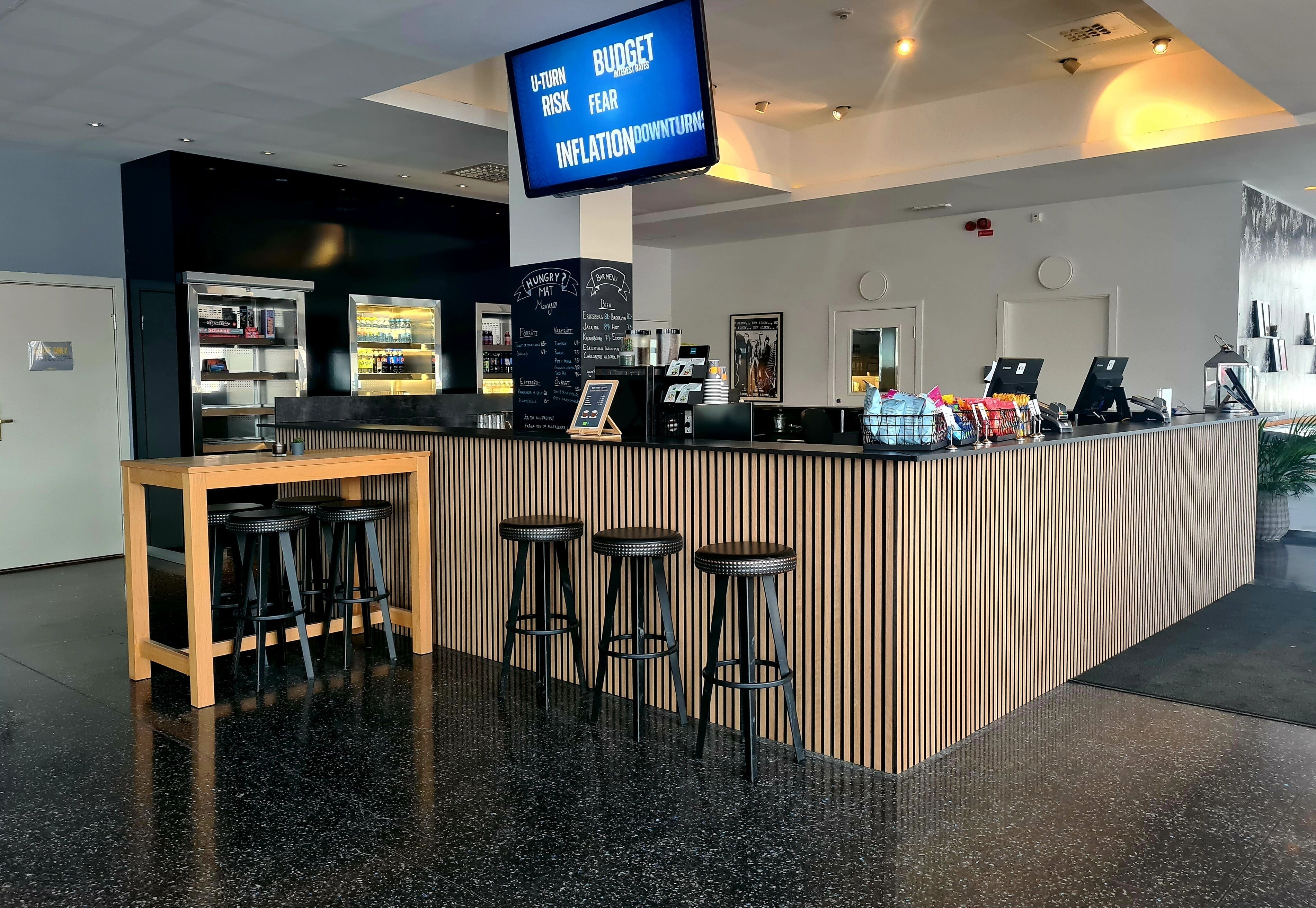 Un área de bar moderna con una pantalla digital que muestra el texto 'U-Turn Risk Budget Fear Inflation Downturn'.