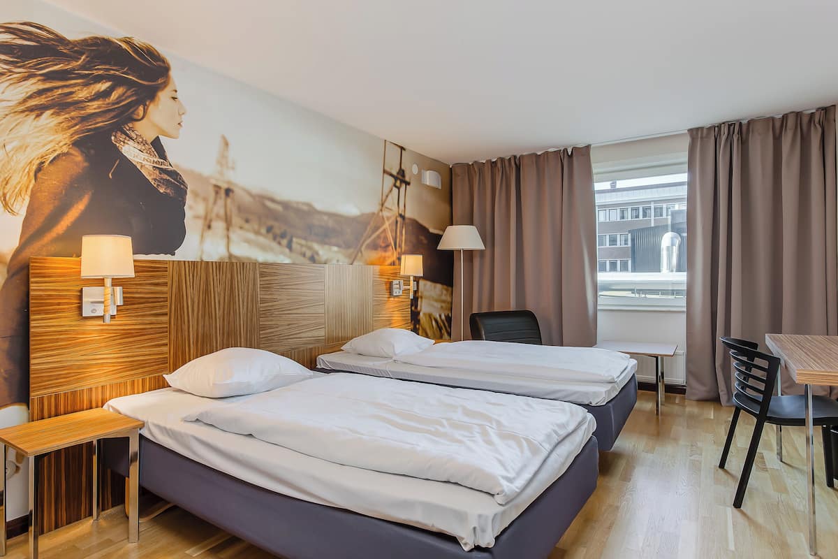 Ein Hotelzimmer mit zwei Betten, einem Schreibtisch, einem Stuhl, einer Lampe und einem großen Gemälde an der Wand.
