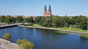 A river with a bridge, a park with trees, and a historic building with two towers in the background.