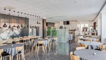 Un restaurante espacioso con mesas y sillas redondas, un gran mural en la pared y un diseño de techo moderno.