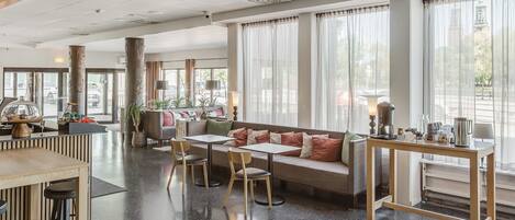 Un moderno vestíbulo de hotel con área de descanso, mostrador de recepción y grandes ventanales.