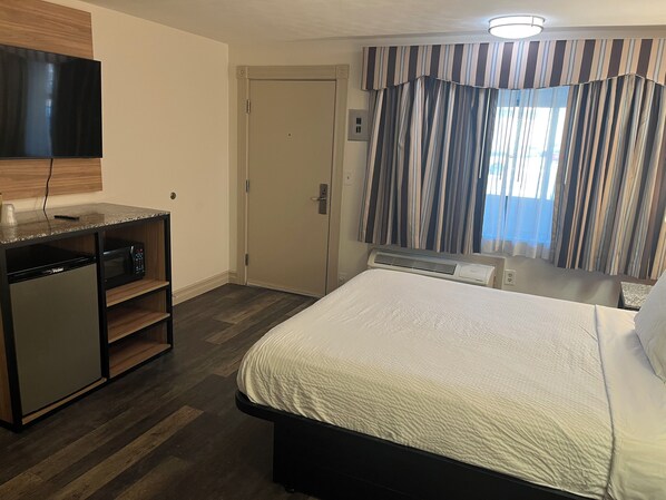 A hotel room with a bed, a desk with a microwave, a television, and a door. - Howard Johnson by Wyndham Malden Boston Area (Malden)