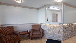 A reception area with a stone wall, two striped armchairs, a small table with a phone, and a doormat with the hotel name. - Howard Johnson by Wyndham Malden Boston Area (Malden)