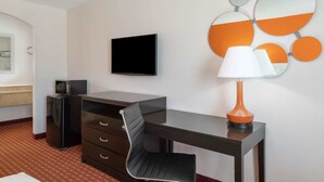 Habitació d'hotel amb escriptori, televisió, microones, nevera, cadira, làmpada i mirall fixat a la paret.