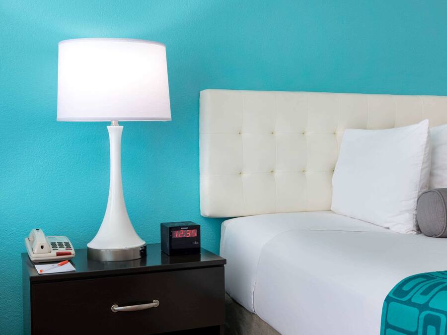 A hotel room with a bed, a nightstand, a lamp, a phone, and a digital clock.