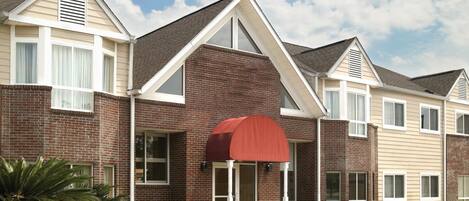 A multi-story hotel with a brick facade, large windows, and a red awning over the entrance.