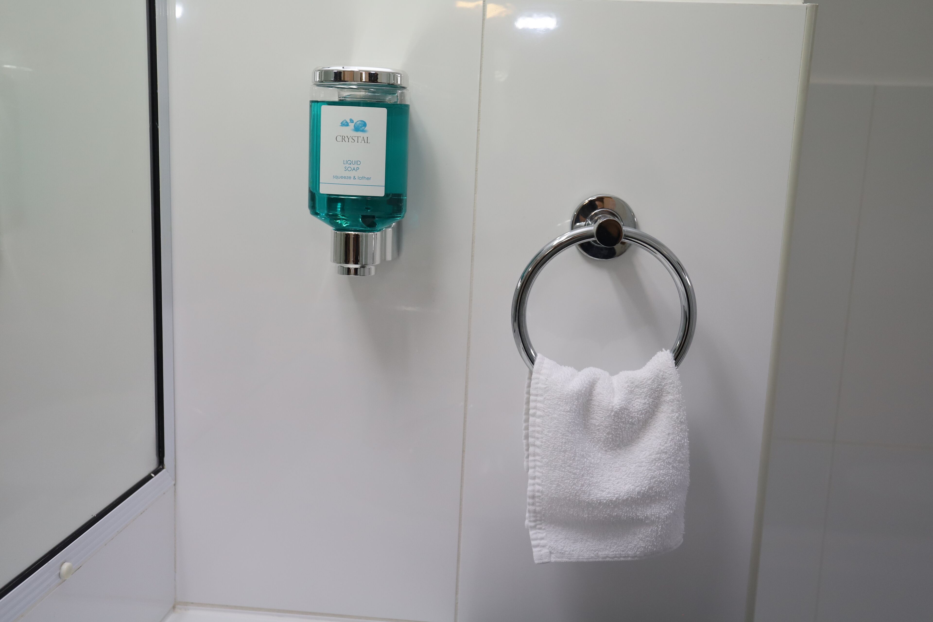 A bathroom with a white tiled wall, a chrome soap dispenser, and a towel ring with a white towel.