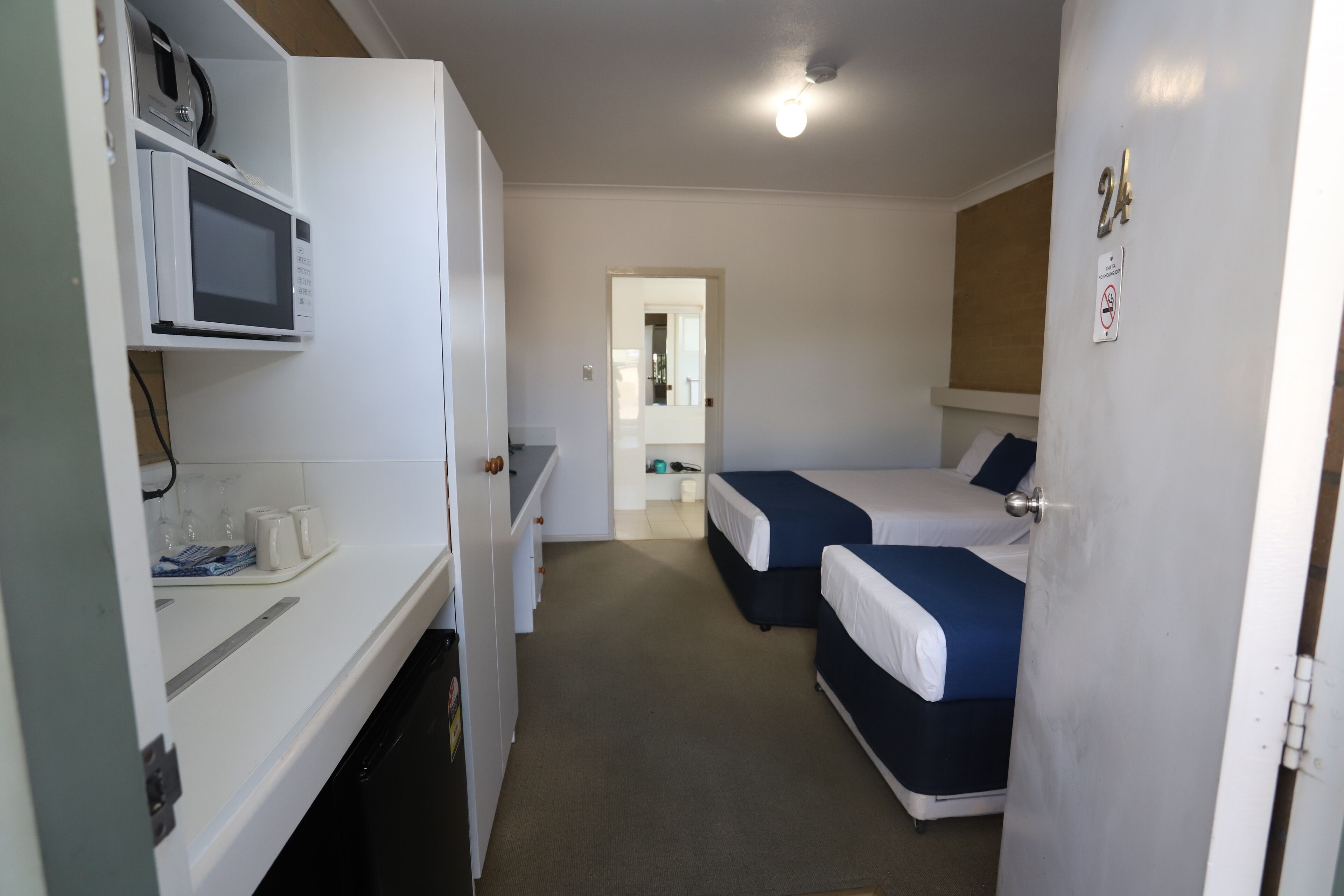 A compact room with a kitchenette, two single beds, and a door leading to another room.