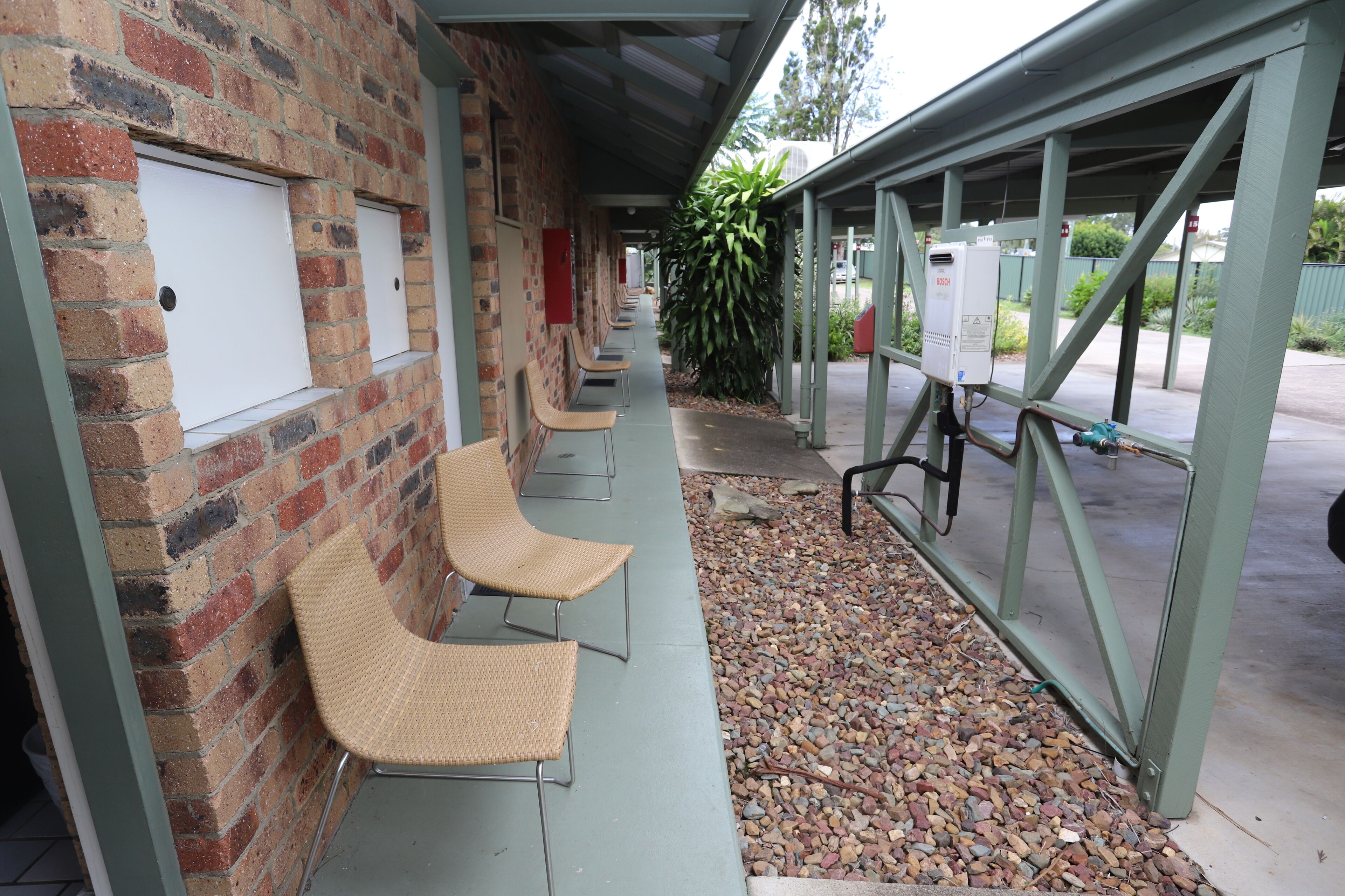 A covered outdoor seating area with wicker chairs and a brick wall.