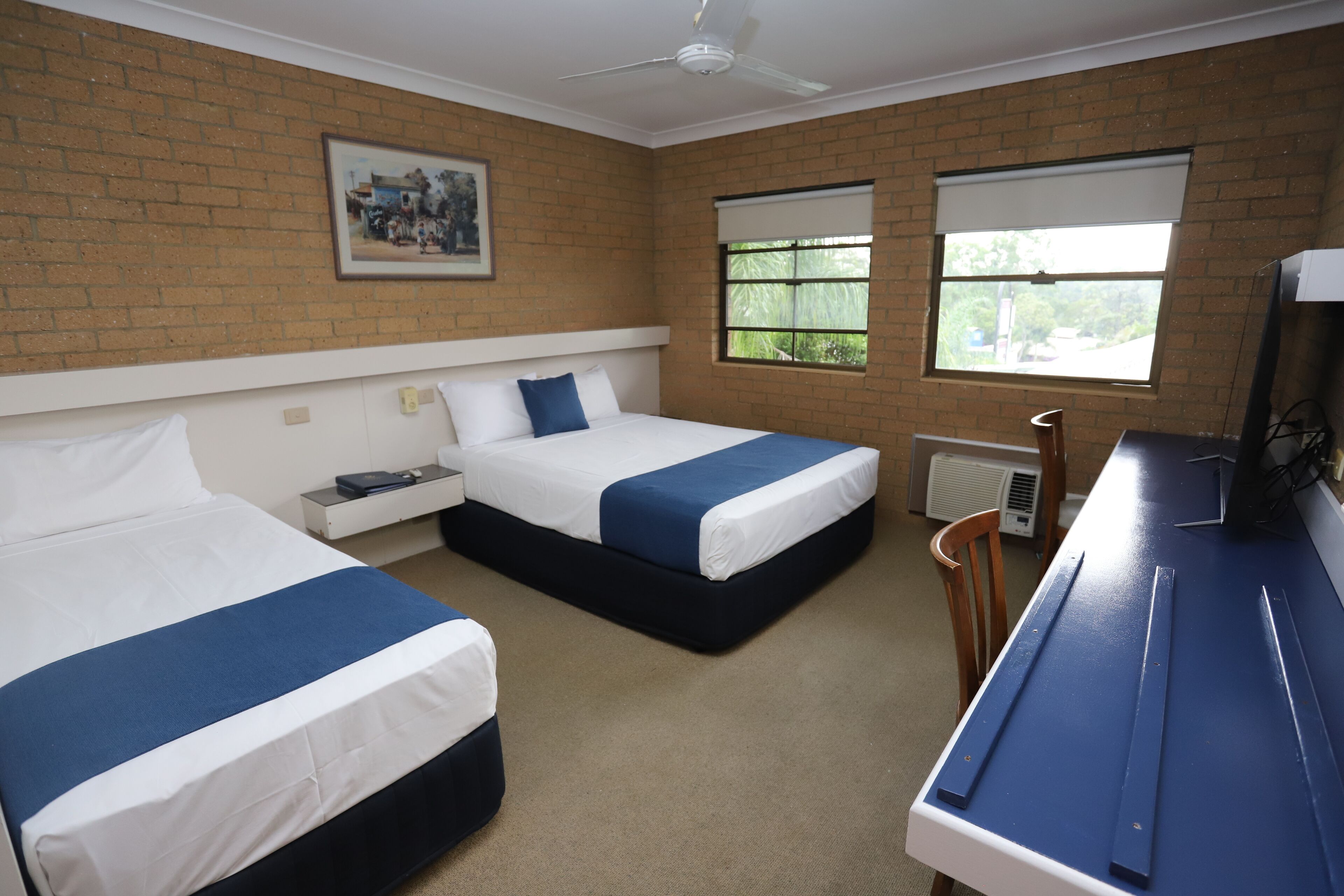 A hotel room with two beds, a desk, and a ceiling fan.