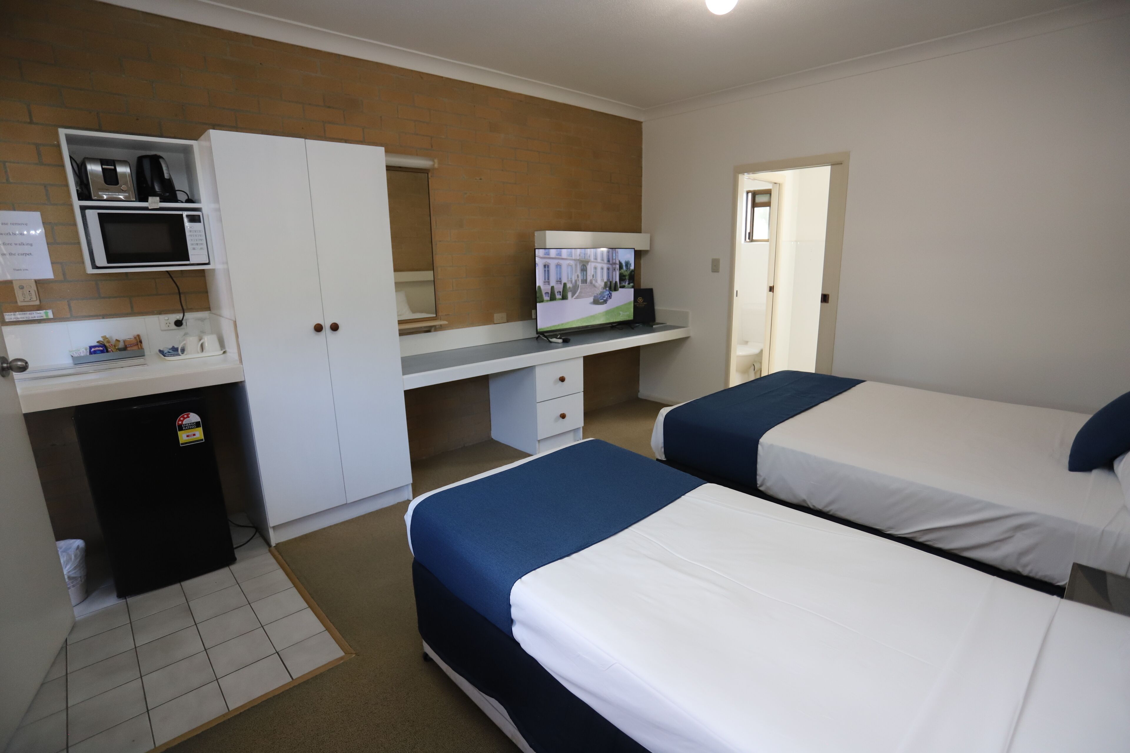 A hotel room with two beds, a desk with a microwave, a refrigerator, and a television.