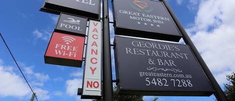 A signpost with multiple signs advertising a motel, pool, free Wi-Fi, and a restaurant.