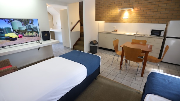 A compact hotel room with a bed, a desk with a computer, a small kitchen area, and a dining table with chairs. - Great Eastern Motor Inn (Monkland)